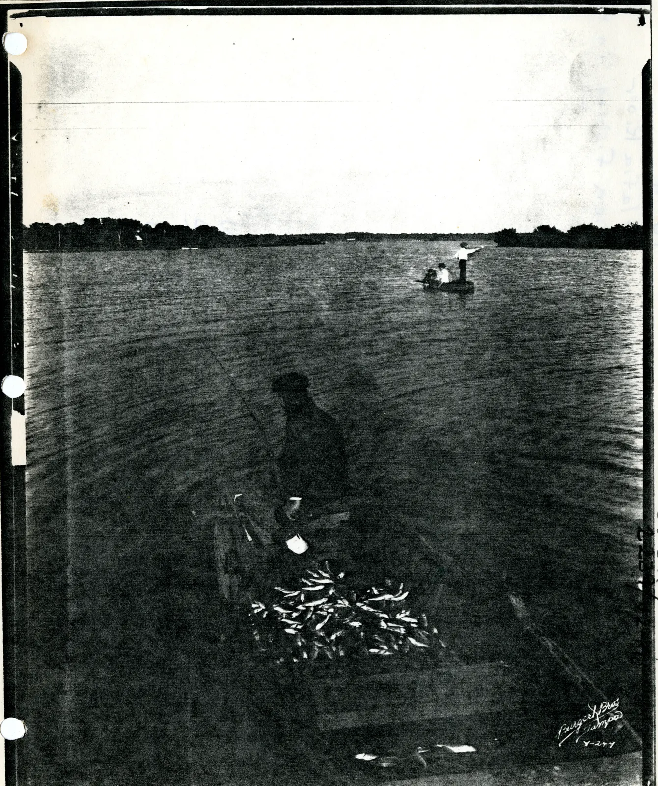 Black-and-white 1920 photo of men in hats fishing from rowboats on the Alafia River, with a wooden dock and trees behind them