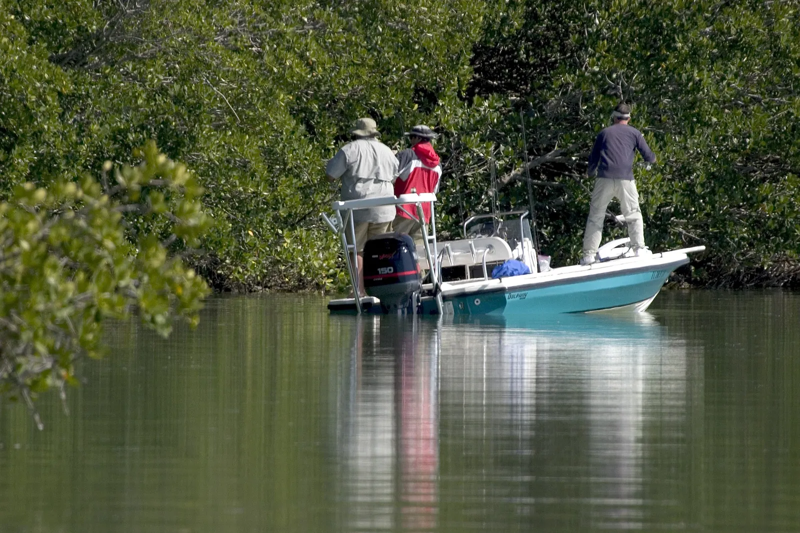 Anglers fishing from a flats skiff along a mangrove shoreline in calm water