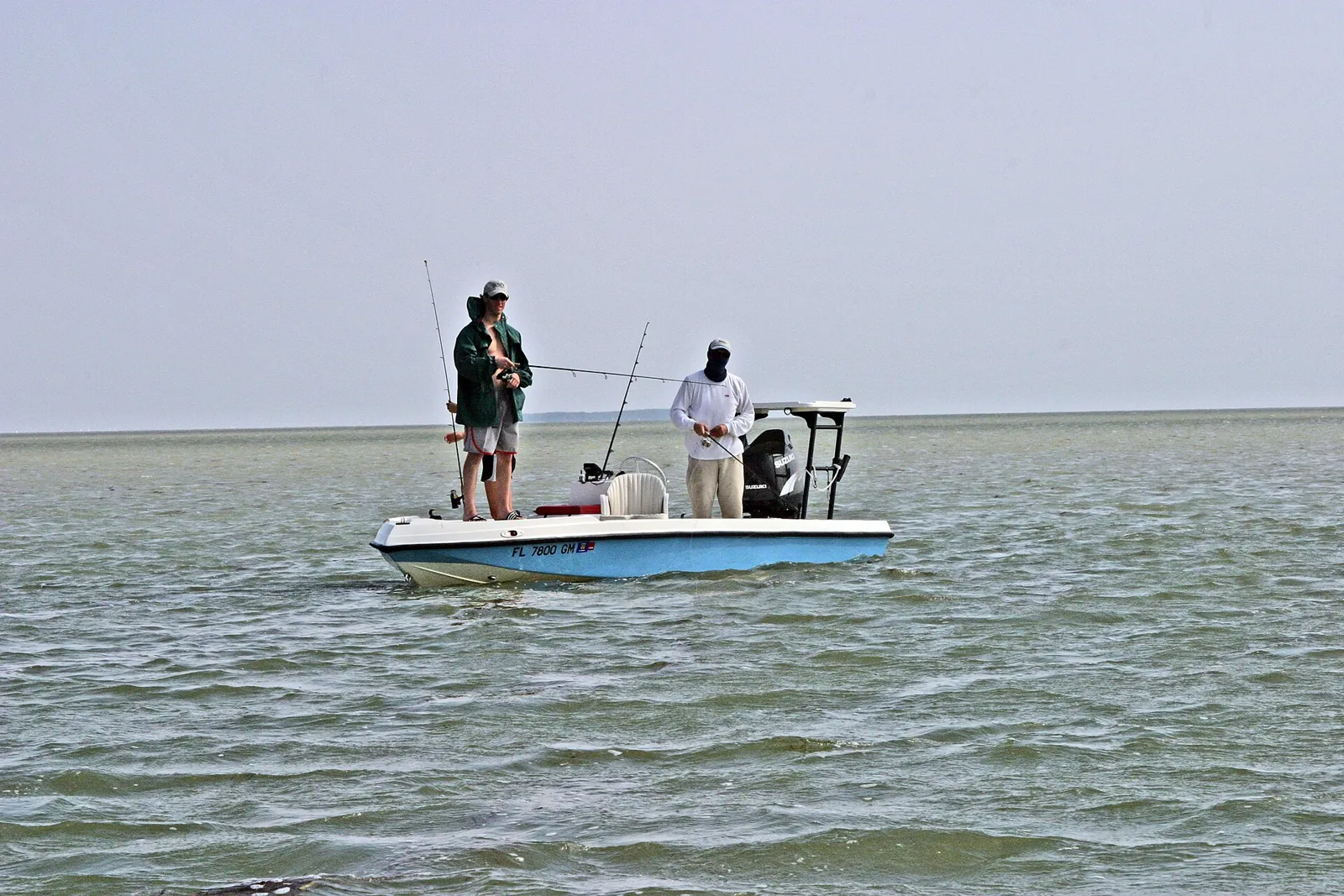 Two anglers casting from a small skiff on open, shallow bay water