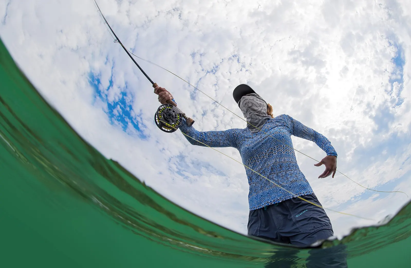 Angler in a long-sleeve sun shirt and face cover fly fishing on shallow flats
