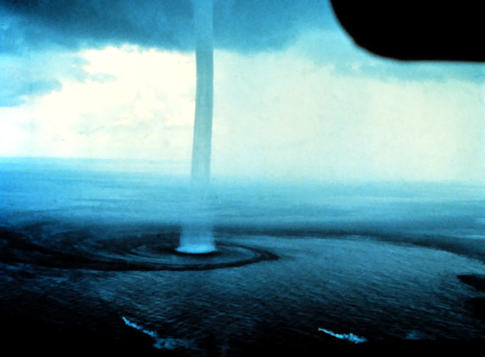 A thin waterspout reaching from dark clouds to the water surface
